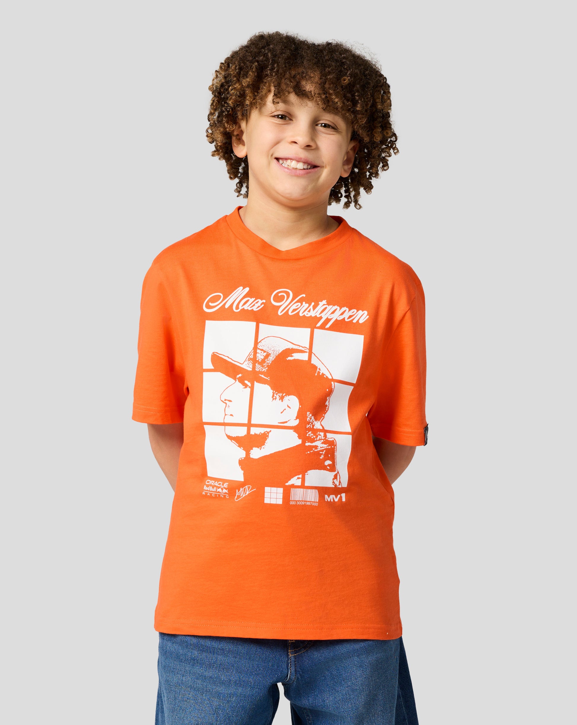 Smiling boy wearing an orange Oracle Red Bull Racing T shirt with a large Max Verstappen graphic on the front.