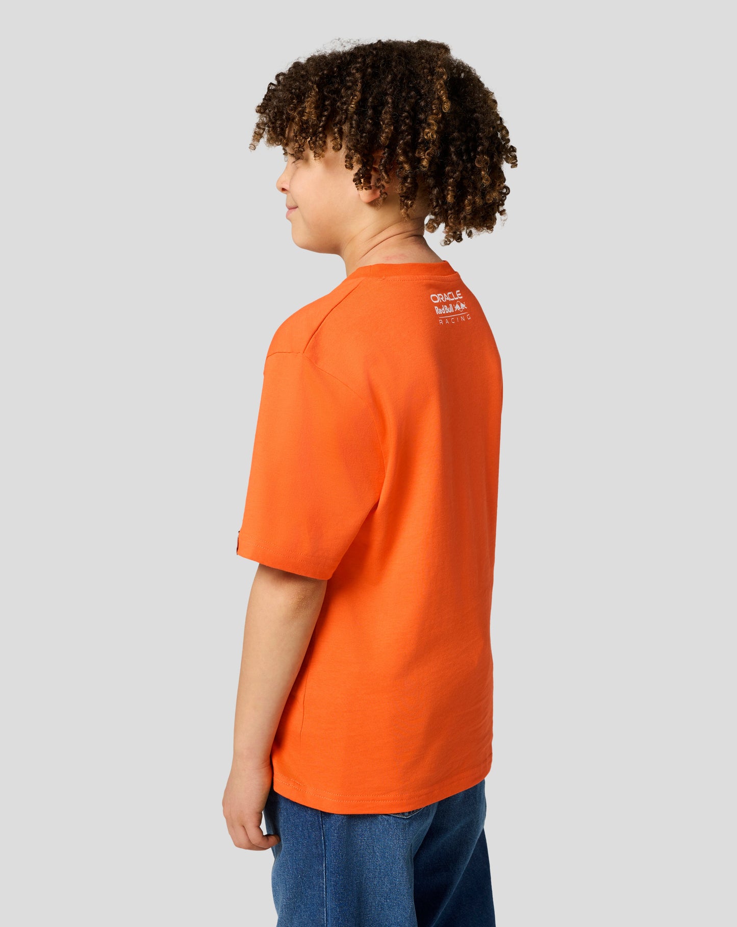 Back view of a child in an orange Max Verstappen T shirt with the Oracle Red Bull Racing logo on the upper back.