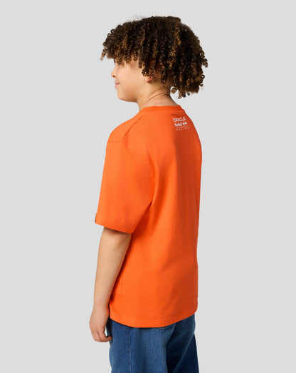 Back view of a child in an orange Max Verstappen T shirt with the Oracle Red Bull Racing logo on the upper back.