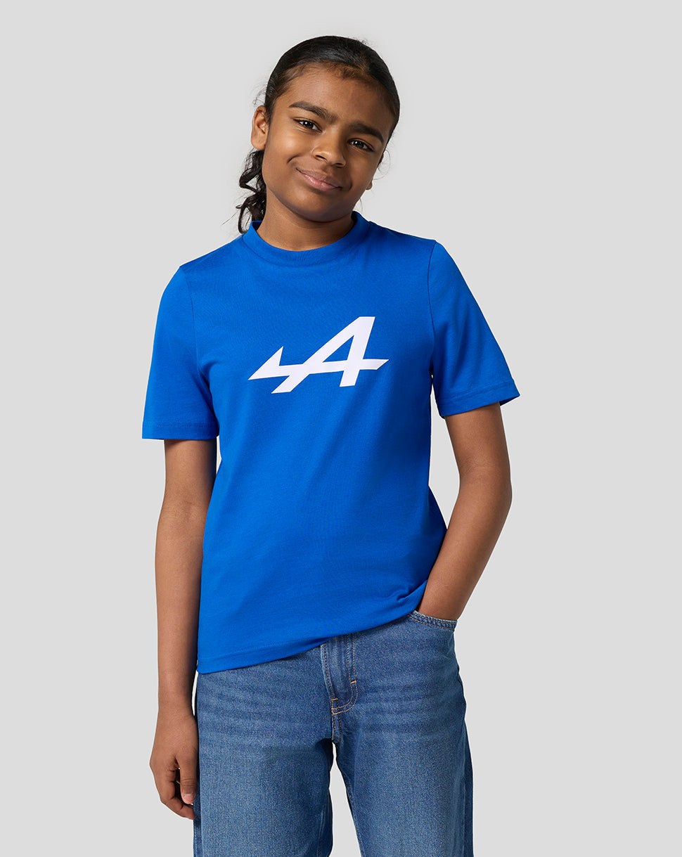 Young girl in lapis blue Alpine Core Essentials T-shirt with white logo, hands in pockets.