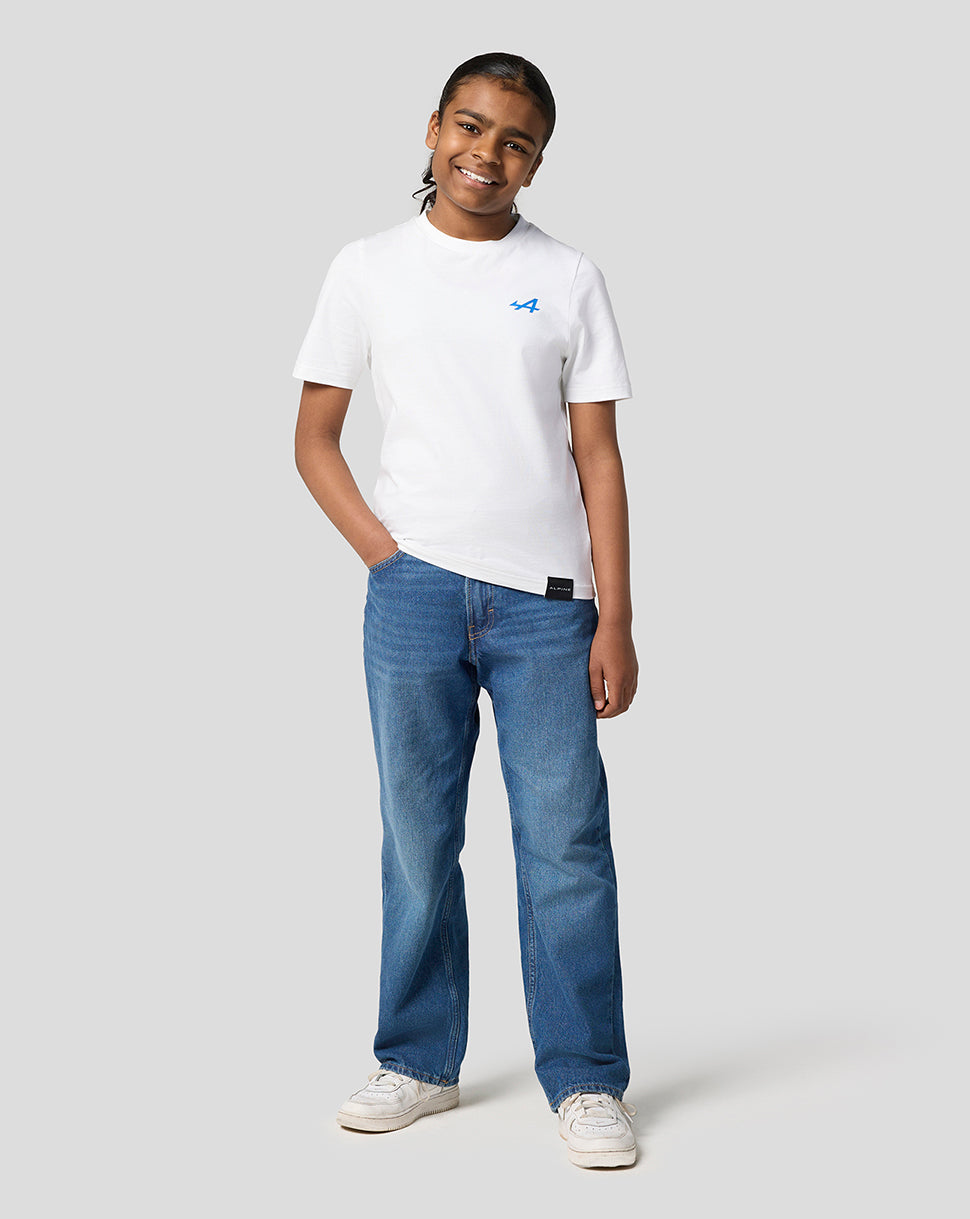 Full body front view of a child in a white Alpine Juniors graphic T shirt with a blue chest logo and denim jeans