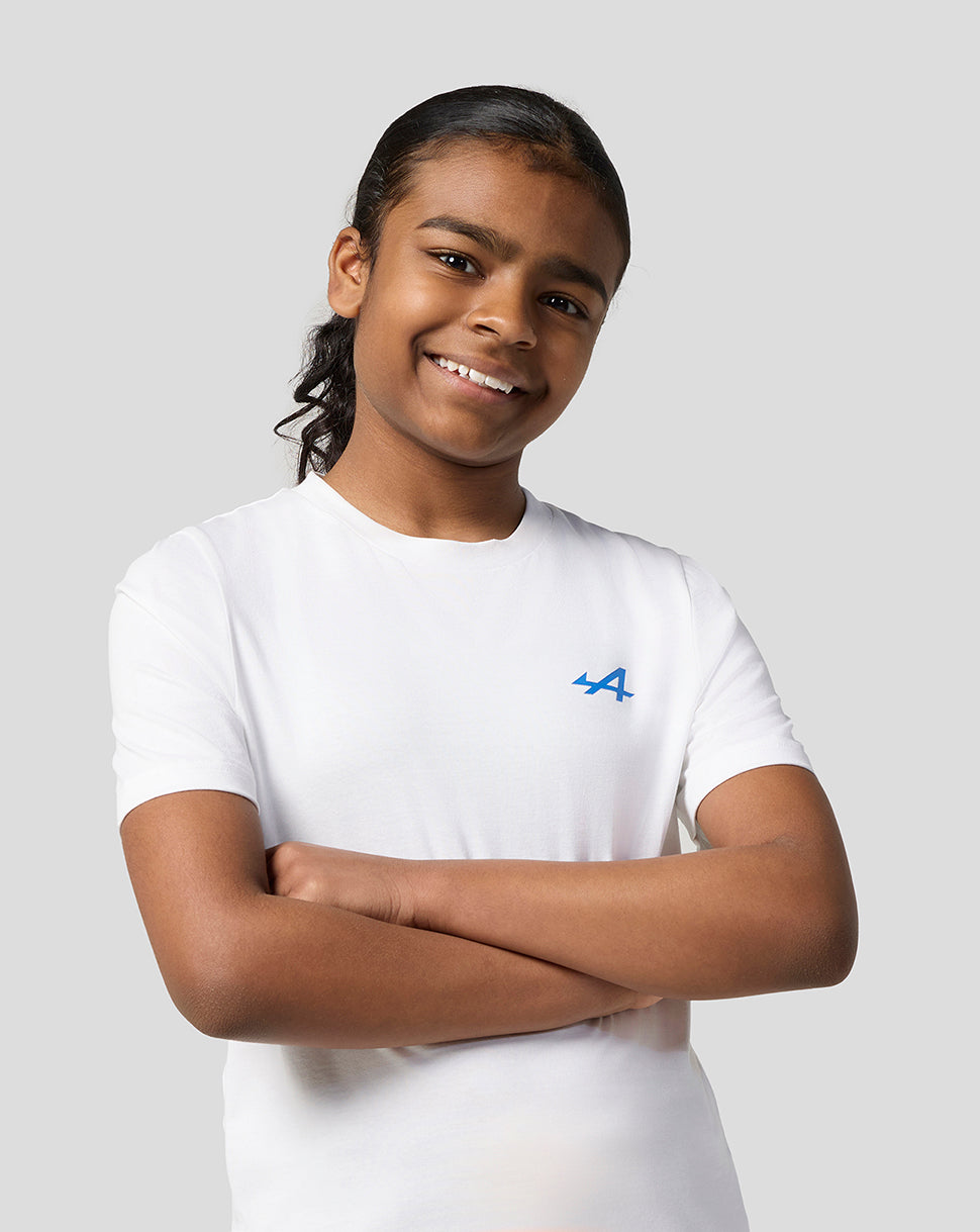 Girl with arms crossed wearing Alpine Juniors white graphic T shirt with blue chest logo.
