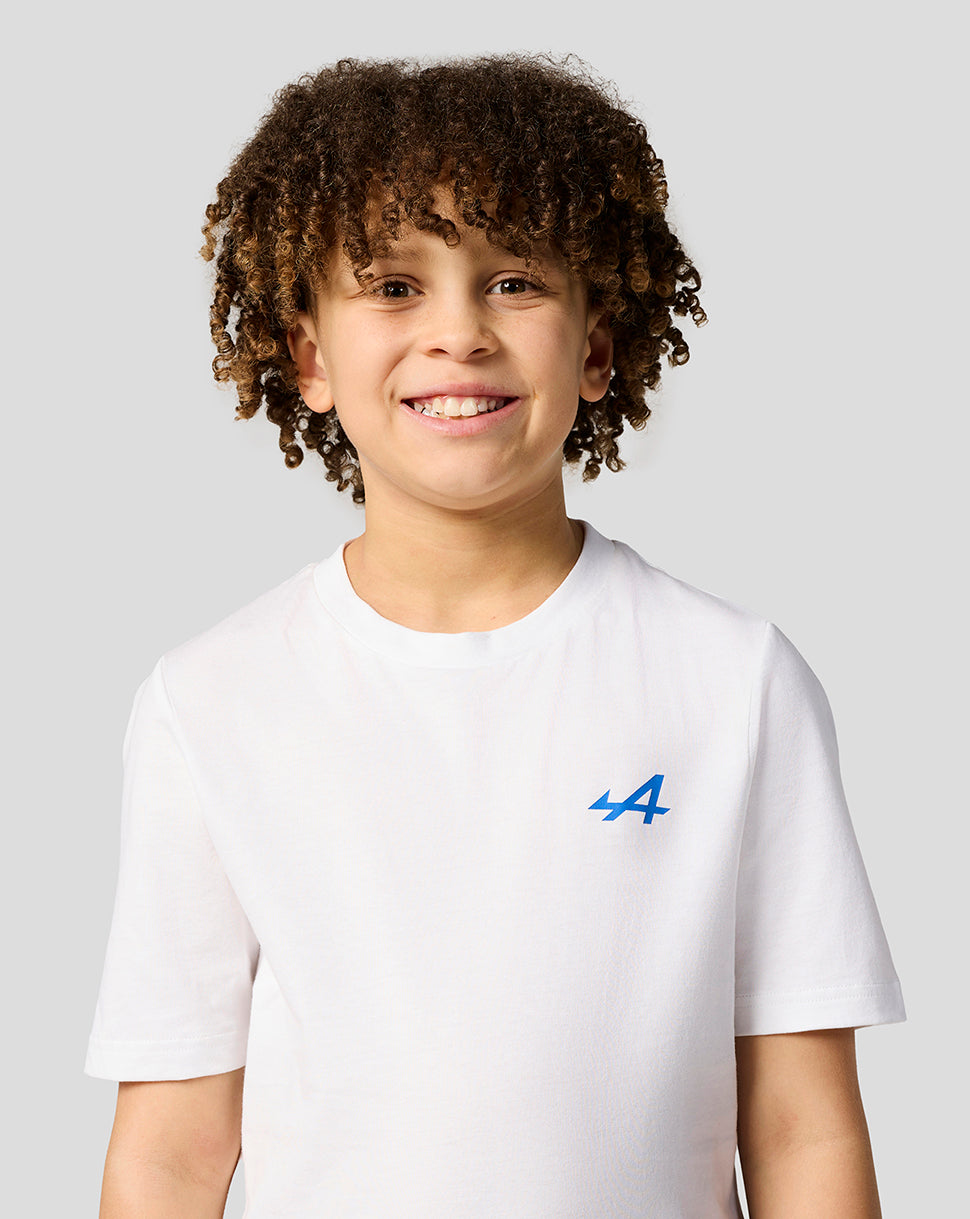 Smiling young girl in a white Alpine Juniors graphic T shirt with blue logo on the left chest.