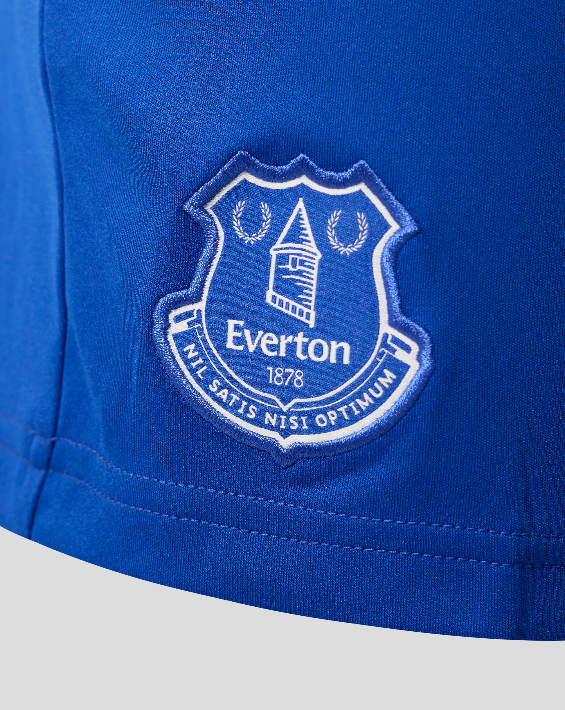 Close-up of blue fabric with an Everton crest patch on junior home shorts