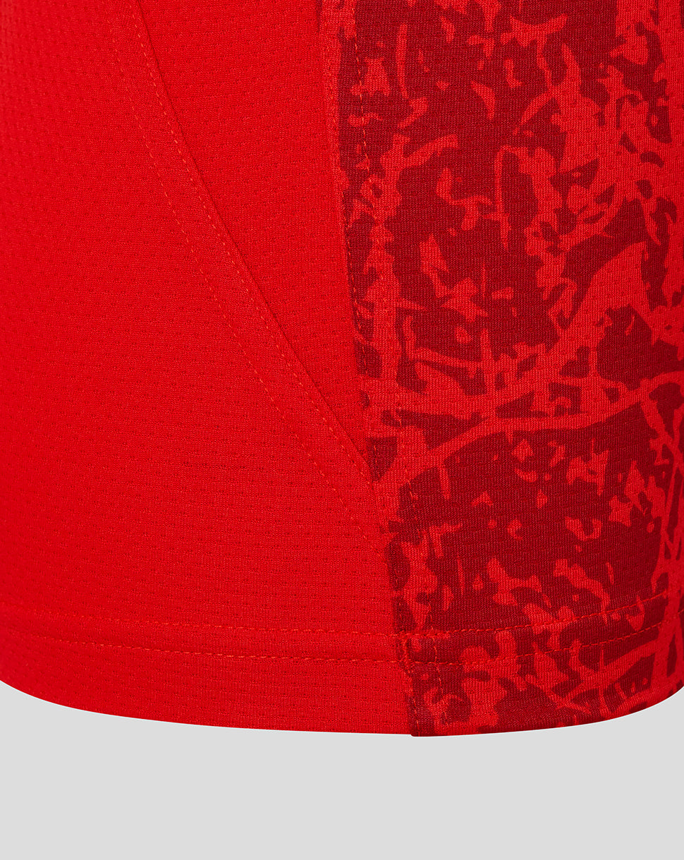 Close up of red textured fabric and abstract camo pattern on the lower front of the Saracens junior matchday tee near the side seam