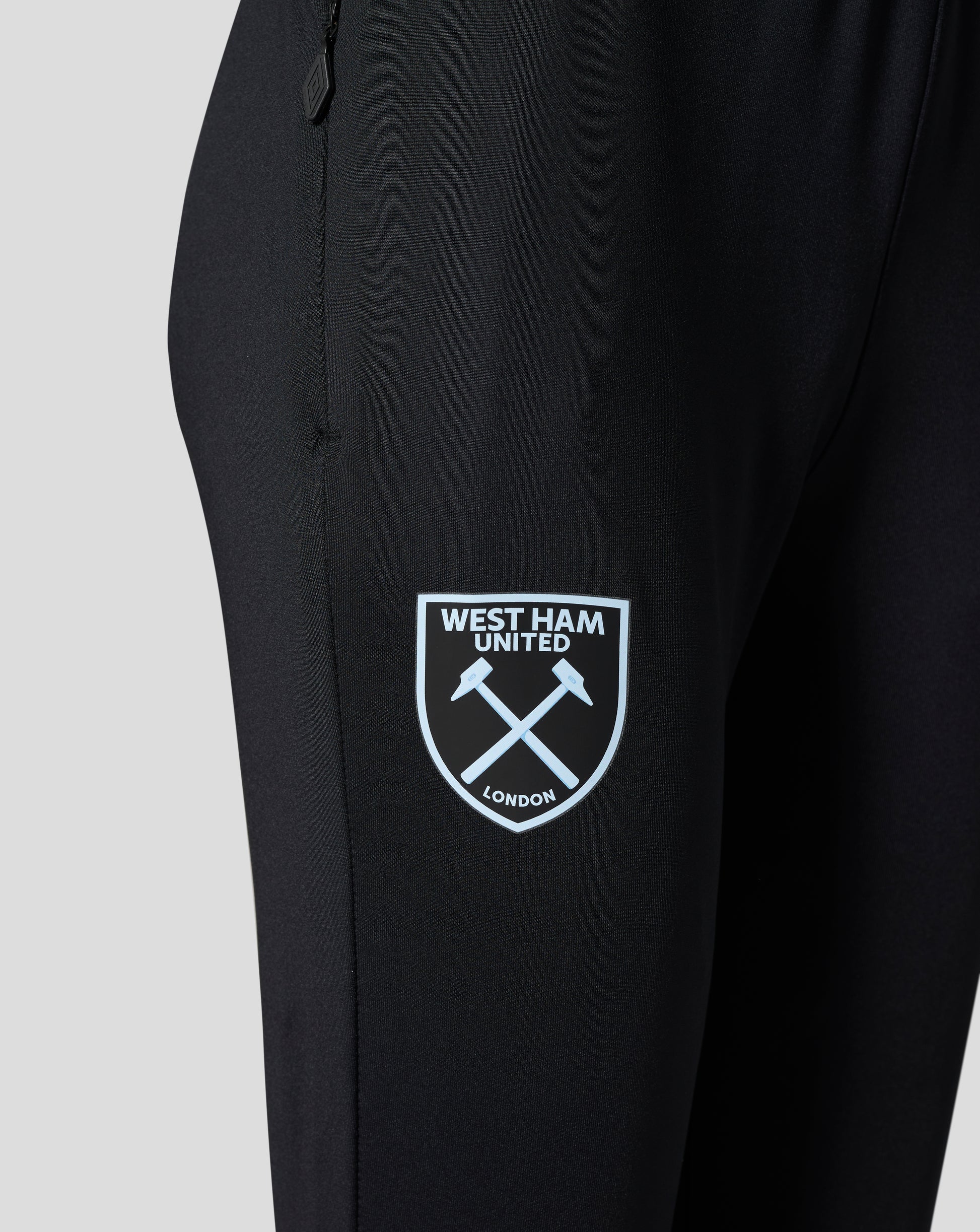 Close-up of black training pants fabric with West Ham United crest patch showing crossed hammers.