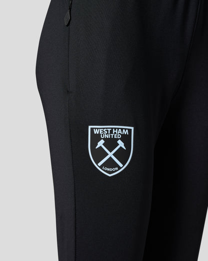 Close-up of black training pants fabric with West Ham United crest patch showing crossed hammers.