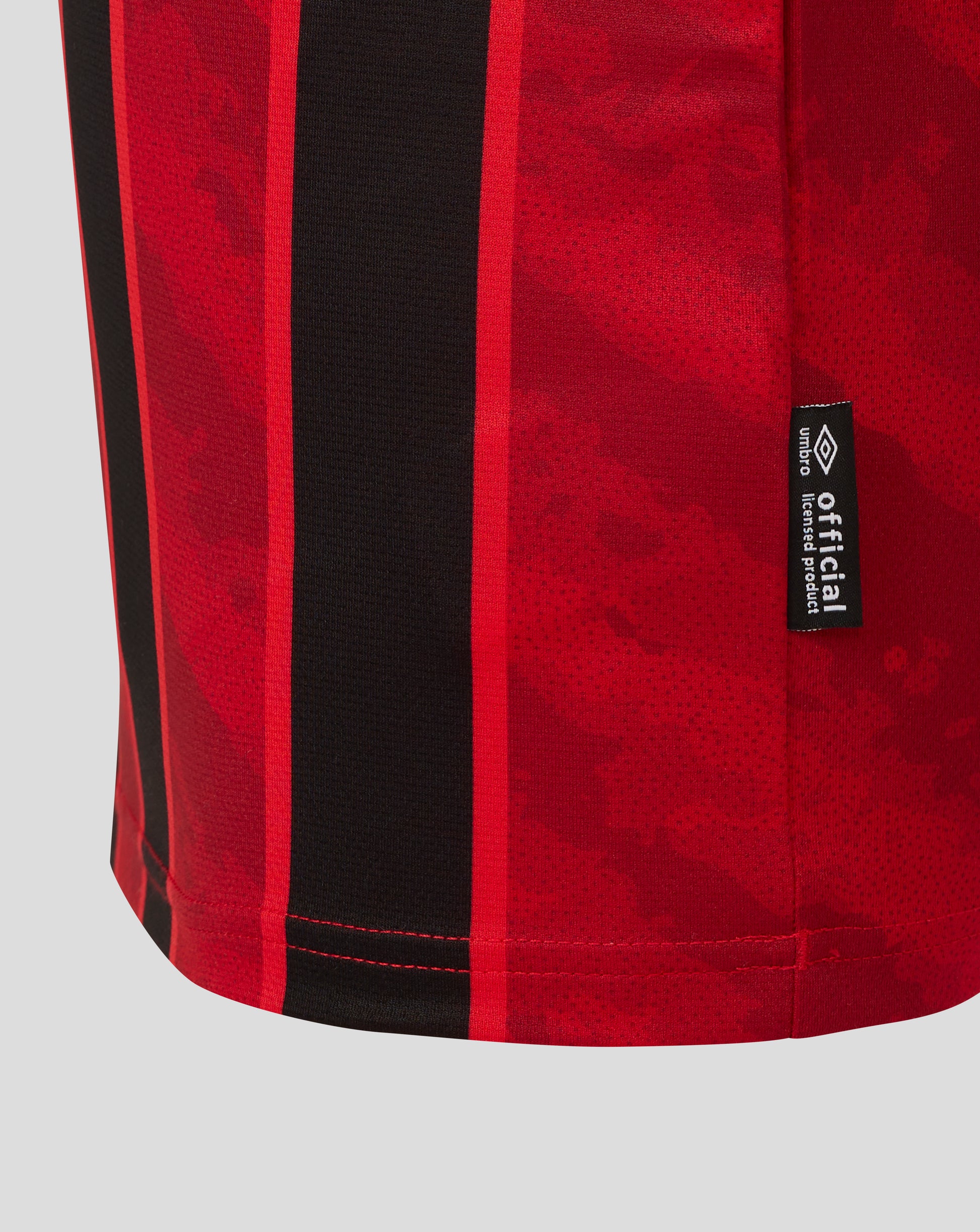 Close up of AFC Bournemouth junior home shirt fabric showing red and black vertical stripes and an official Umbro tag.