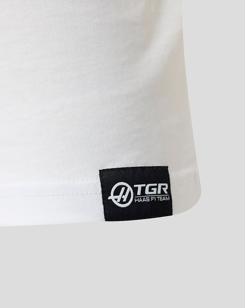 Close-up of a white shirt with a black TGR logo tag on a light gray background