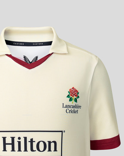 Cream Lancashire junior jersey front left chest showing Lancashire Cricket crest and Hilton sponsor across mid chest.