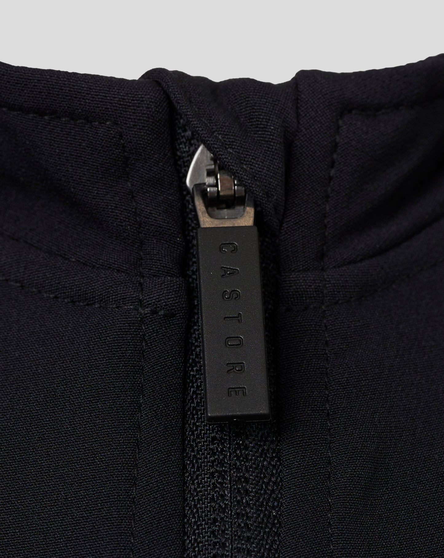Close-up of zipper at the neckline of a black Castore jacket showing textured fabric and branding