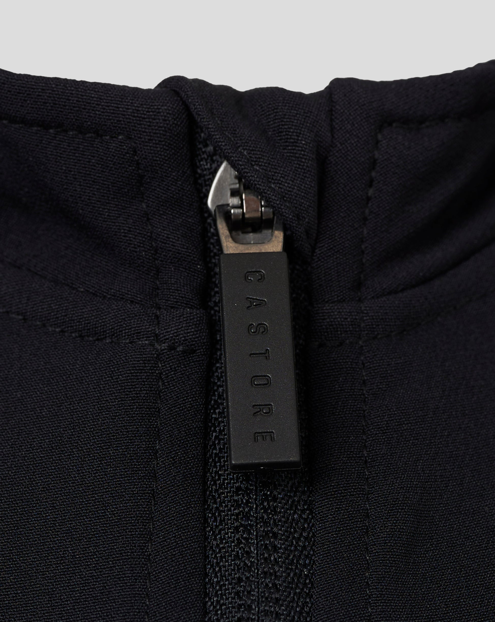 Close-up of zipper at the neckline of a black Castore jacket showing textured fabric and branding