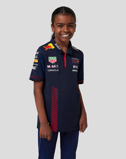 Junior girl wearing navy Castore x Oracle Red Bull Racing polo with heat transfer sponsor logos.