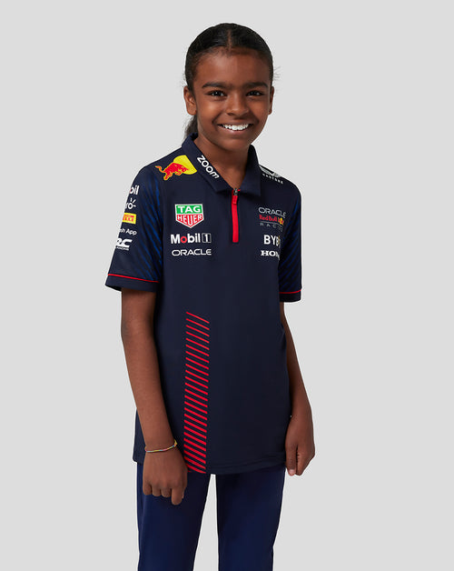 Junior girl wearing navy Castore x Oracle Red Bull Racing polo with heat transfer sponsor logos.