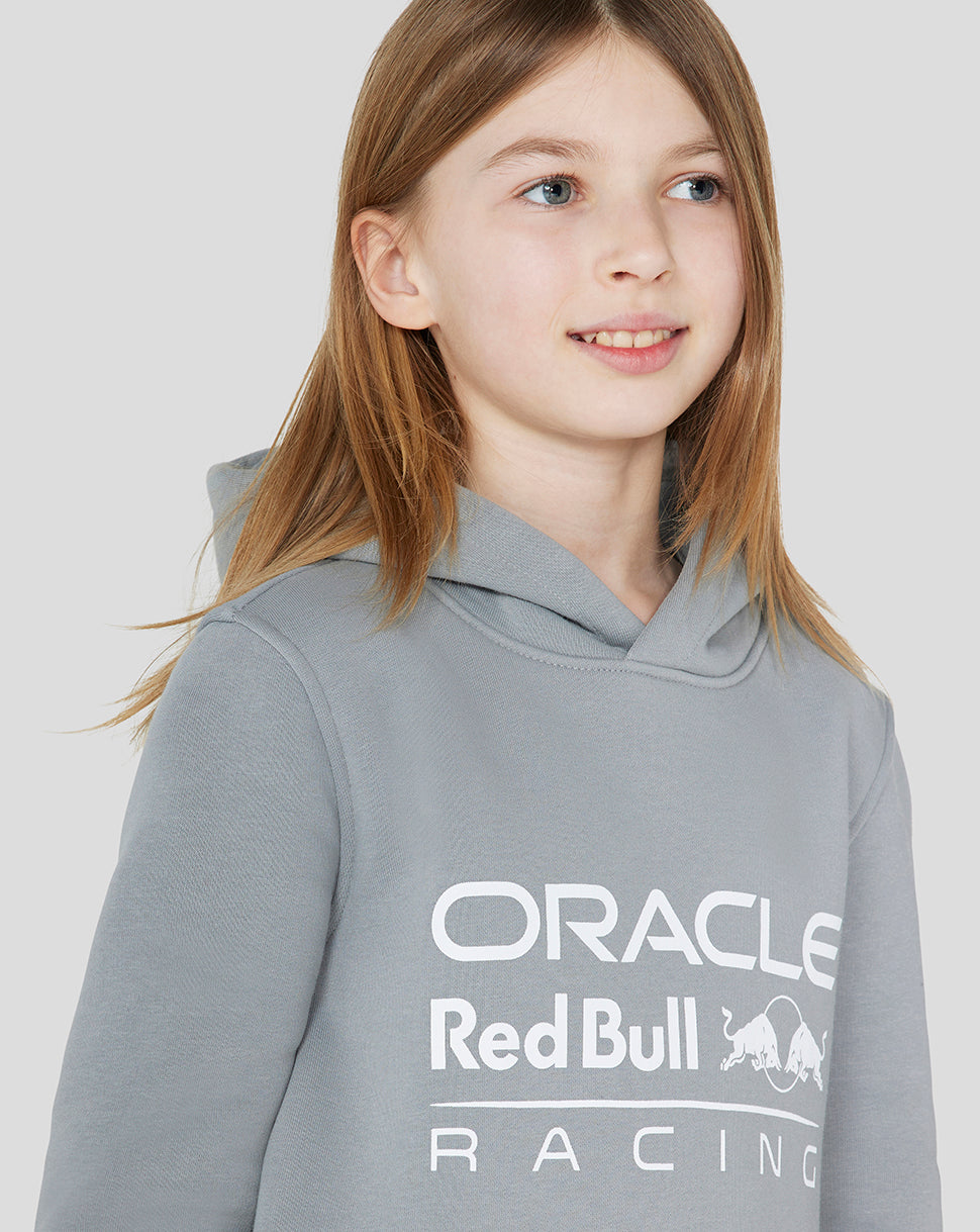 Front view of a smiling girl wearing a grey Oracle Red Bull Racing Junior Core Overhead Hoodie with a large chest logo.