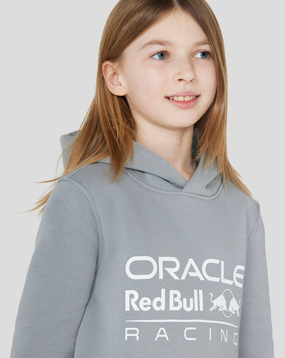 Front view of a smiling girl wearing a grey Oracle Red Bull Racing Junior Core Overhead Hoodie with a large chest logo.