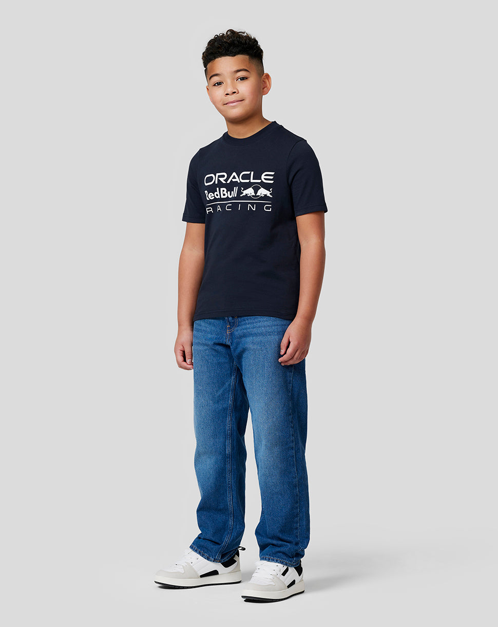 Full-length shot of a boy in a navy Oracle Red Bull Racing T shirt with a large front logo, jeans and sneakers.