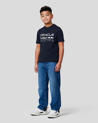 Full-length shot of a boy in a navy Oracle Red Bull Racing T shirt with a large front logo, jeans and sneakers.