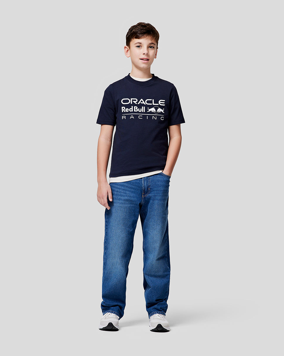 Full-length shot of a boy wearing a navy Oracle Red Bull Racing junior large front logo T shirt with jeans.