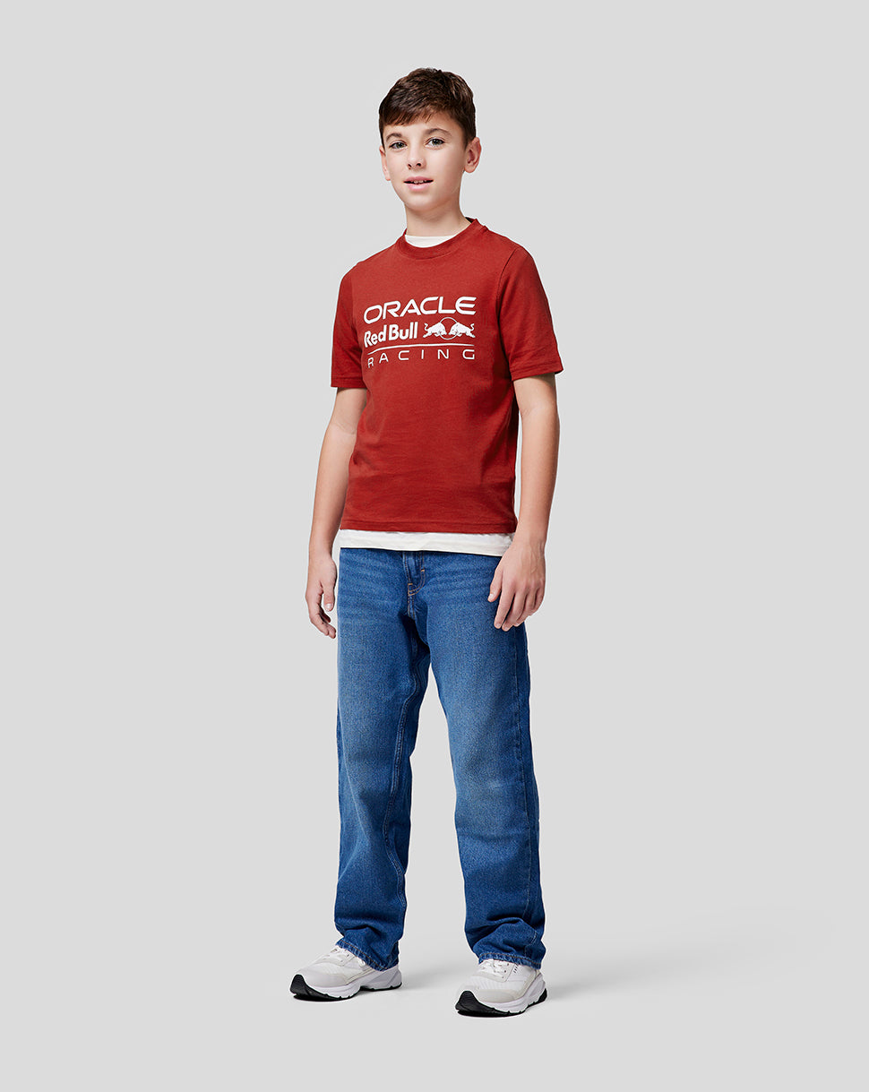 Full body shot of a boy in a red Oracle Red Bull Racing juniors tee with the logo across the chest, jeans and white sneakers