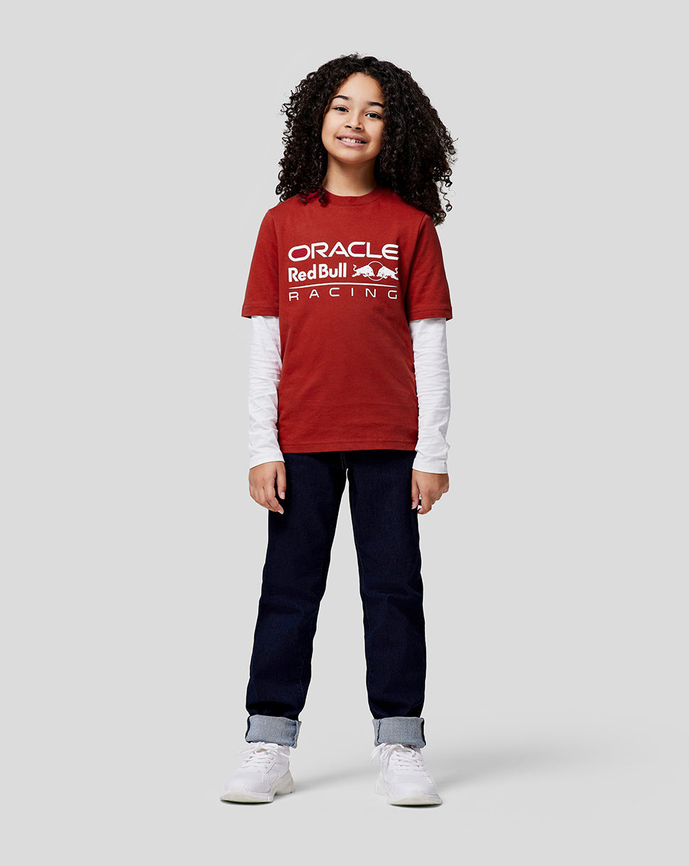 Curly haired girl in a red Oracle Red Bull Racing T shirt over a white long sleeve, smiling.