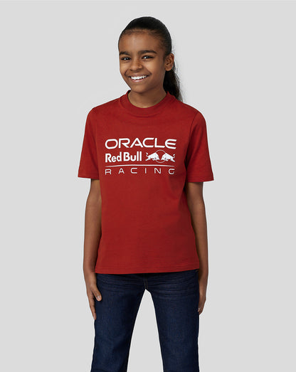 Front view of a smiling girl wearing a red Oracle Red Bull Racing juniors T shirt with large logo on the chest and jeans