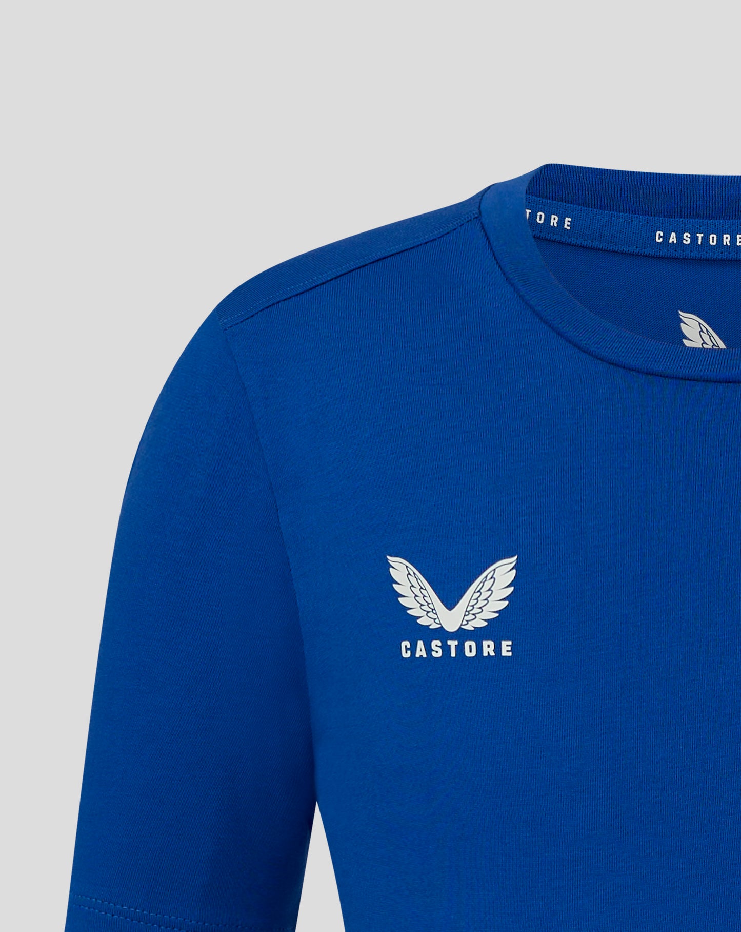 Blue junior cotton leisure tee close up showing self fabric crew neck and forward shoulder seam with Castore wing logo