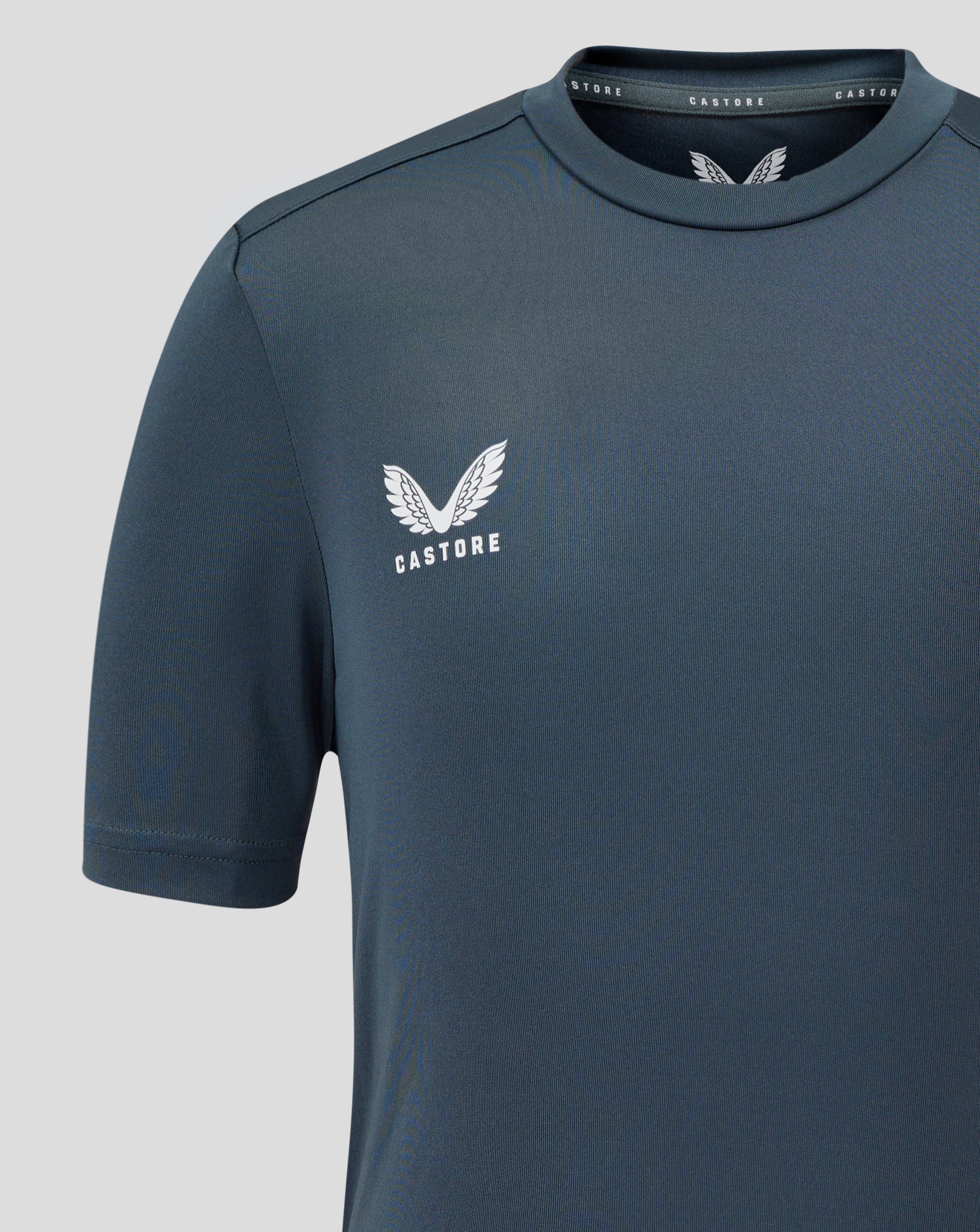 Dark slate junior performance tee with crew neck and short sleeves showing a white Castore wing logo on the chest.