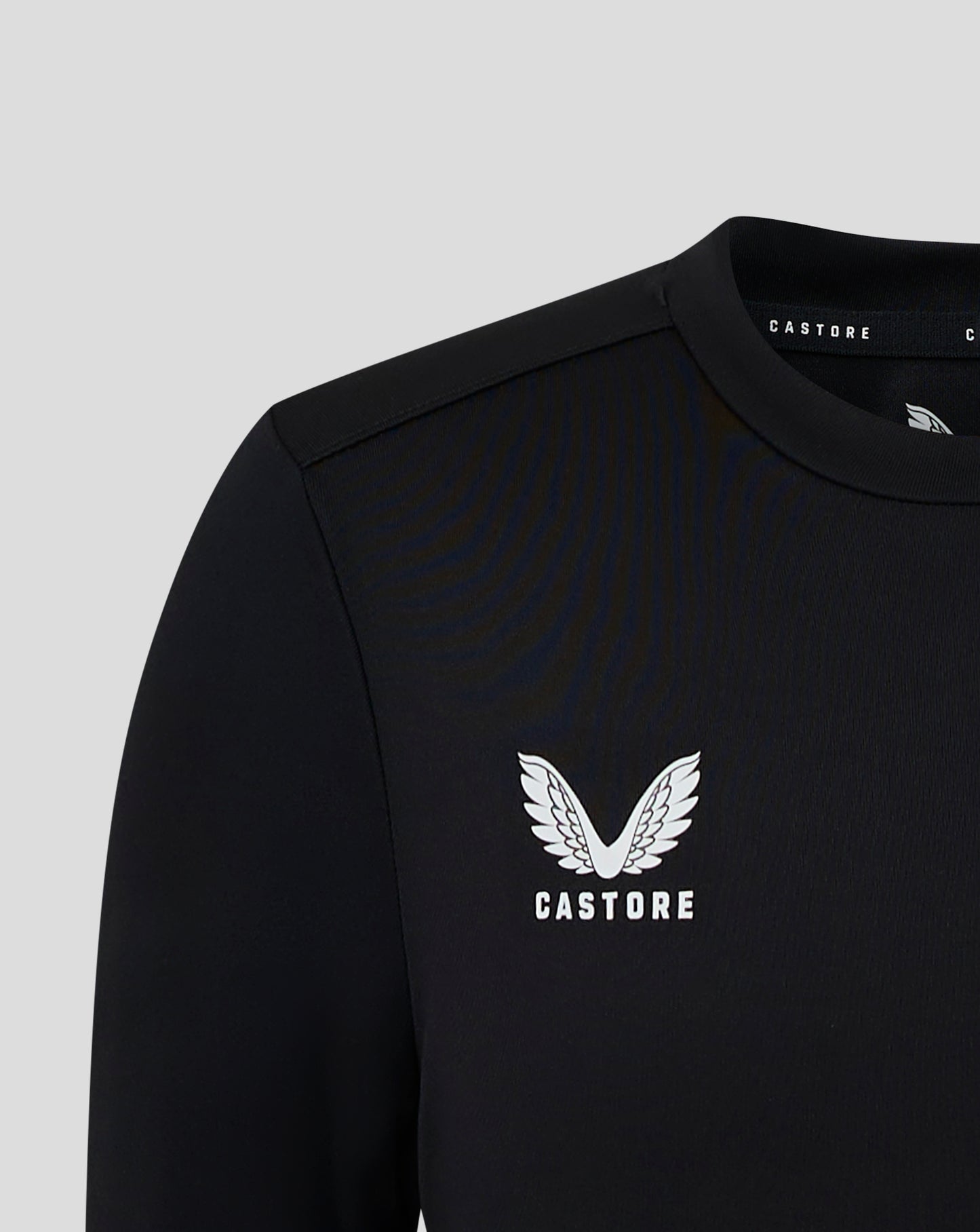 Close-up of a black junior long sleeve performance tee showing a white Castore crest on the chest and neck label