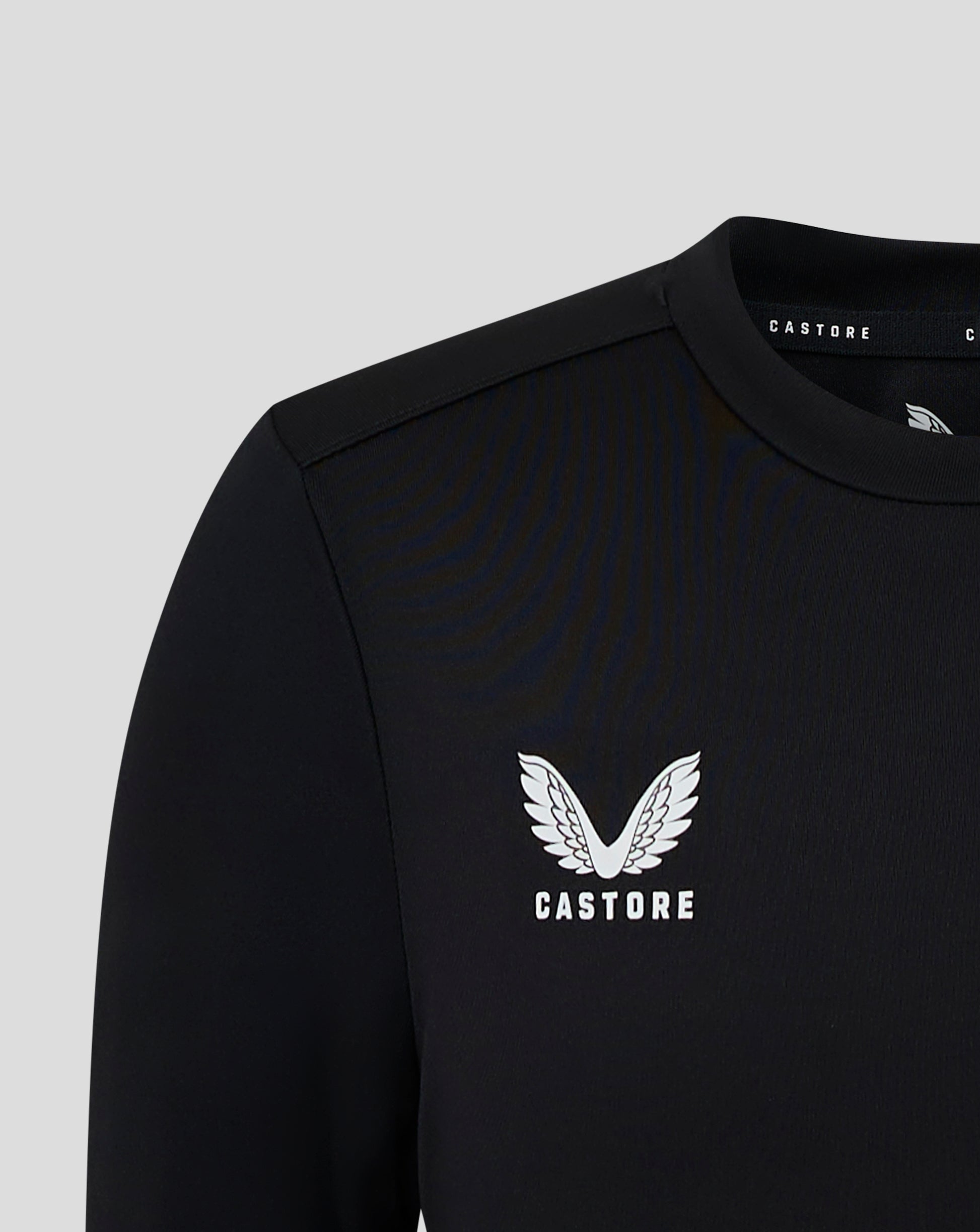 Close-up of a black junior long sleeve performance tee showing a white Castore crest on the chest and neck label