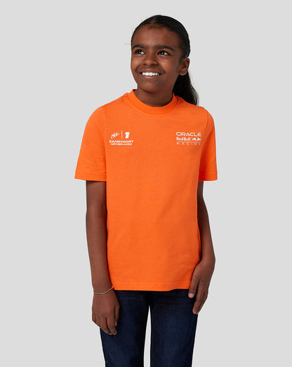 Front view of a child in an orange Oracle Red Bull Racing junior T shirt with Verstappen graphic on the front and branding on the chest.