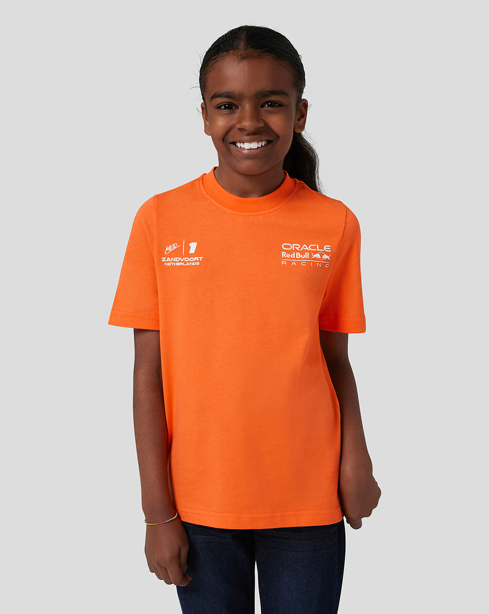 Young girl wearing a bright orange Oracle Red Bull Racing Junior T Shirt with Verstappen graphics on front and back and the left chest logo