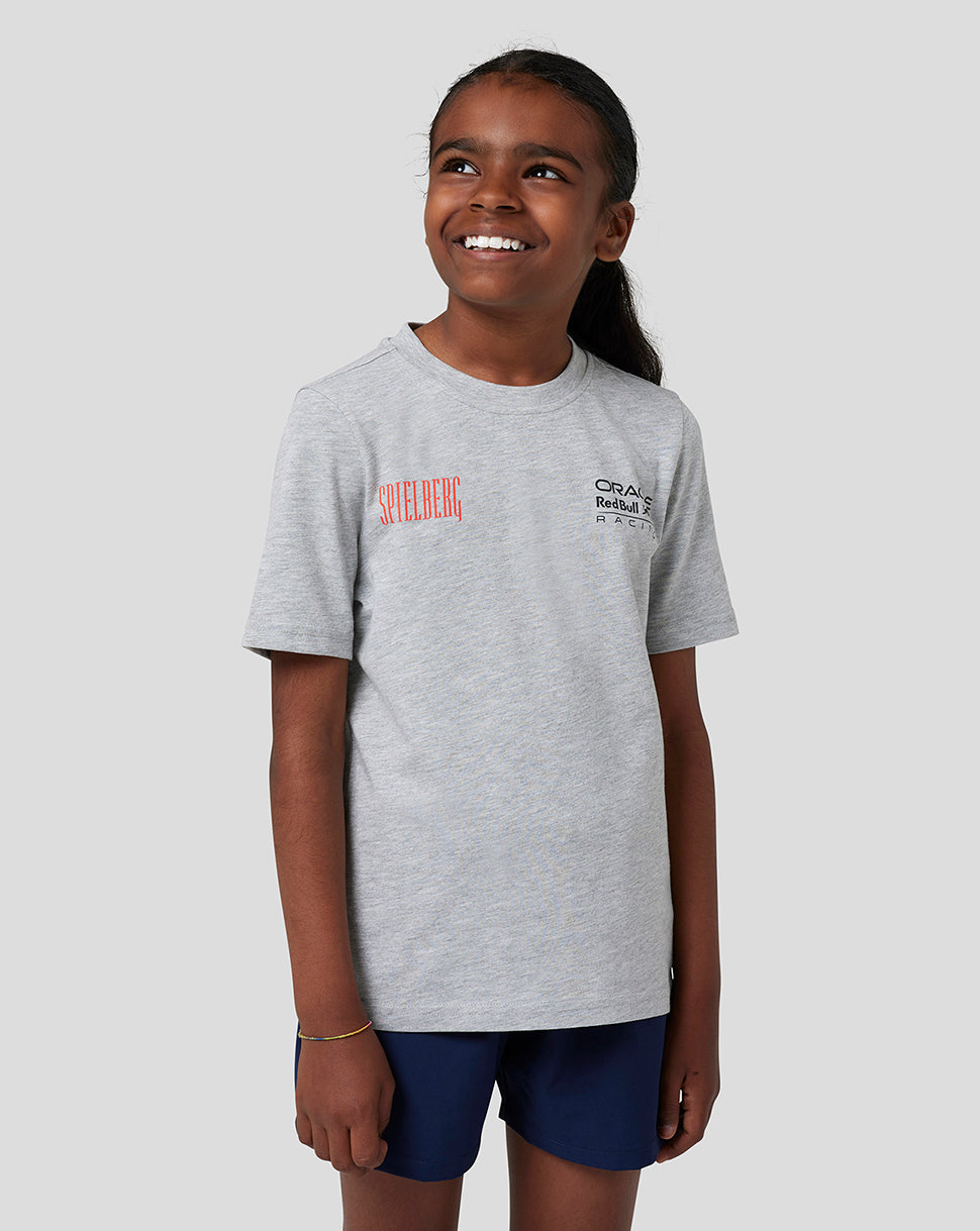 Front view of a smiling girl wearing a grey marl Red Bull Racing Junior Spielberg T-Shirt with red Spielberg wording and Oracle logo on the chest
