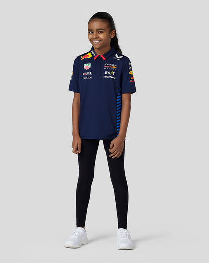 Full length shot of a child in a navy Oracle Red Bull Racing Teamline polo with blue striped panels black leggings and white sneakers