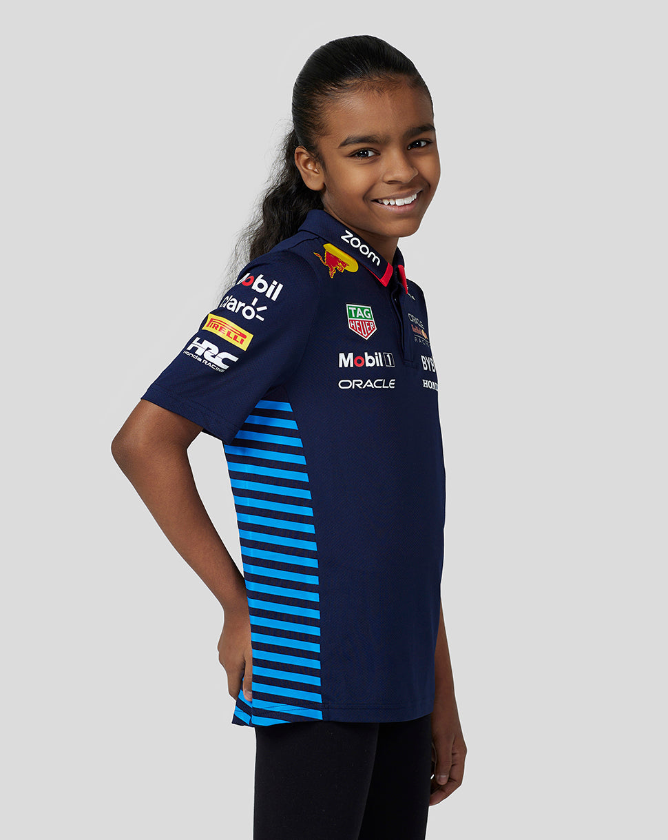 Side view of a young girl wearing a navy Oracle Red Bull Racing Teamline polo with blue striped side panels and sponsor logos