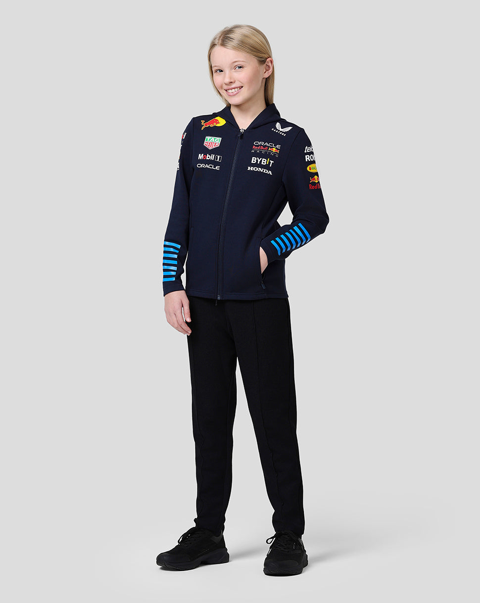 Full-body front view of a girl wearing a navy Red Bull team hoodie with multiple sponsor logos on the chest and blue striped cuffs.