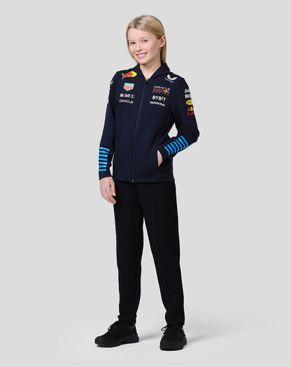 Full-body front view of a girl wearing a navy Red Bull team hoodie with multiple sponsor logos on the chest and blue striped cuffs.