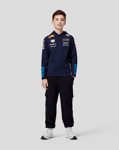 Front view of a young racer wearing navy teamline hoodie with chest logos blue striped sleeves black cargo pants and white sneakers.