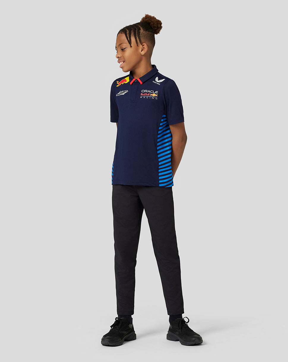 Front view of a smiling young boy wearing a navy Max Verstappen Teamline polo with sponsor logos and blue side stripes