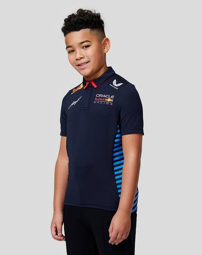 Young boy wearing a navy Checo Teamline polo with blue stripe detailing and multiple sponsor logos.