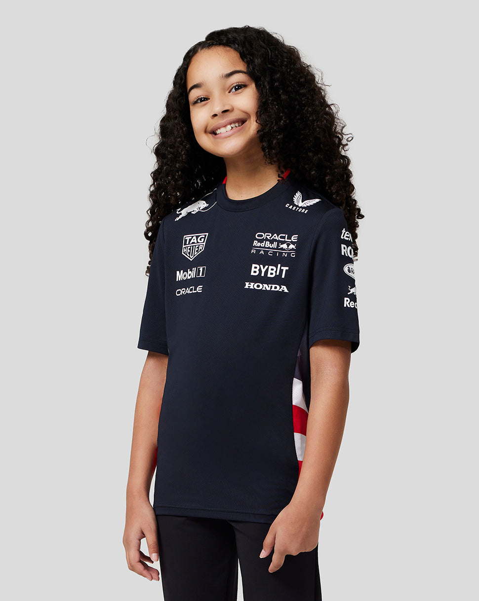 Smiling child wearing a navy Oracle Red Bull Racing Junior Teamline America T Shirt with sponsor logos on chest and sleeves