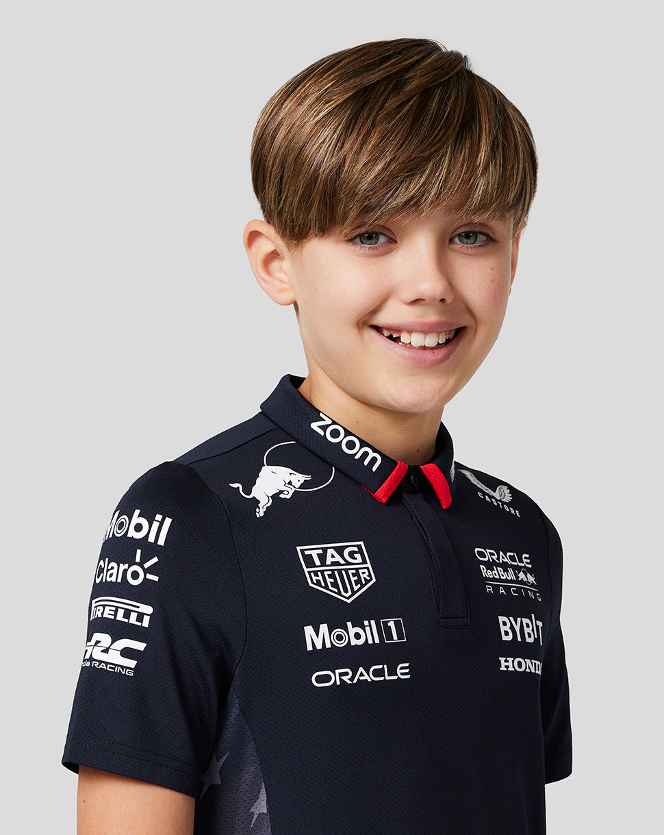 Smiling boy wearing a Night Sky navy Oracle Red Bull Racing Junior Teamline polo with sponsor logos.