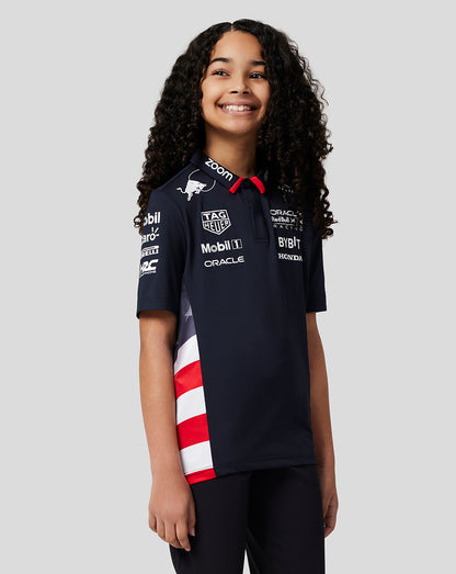 Smiling girl wearing a navy junior America Race Team polo with a red collar and striped side panel.
