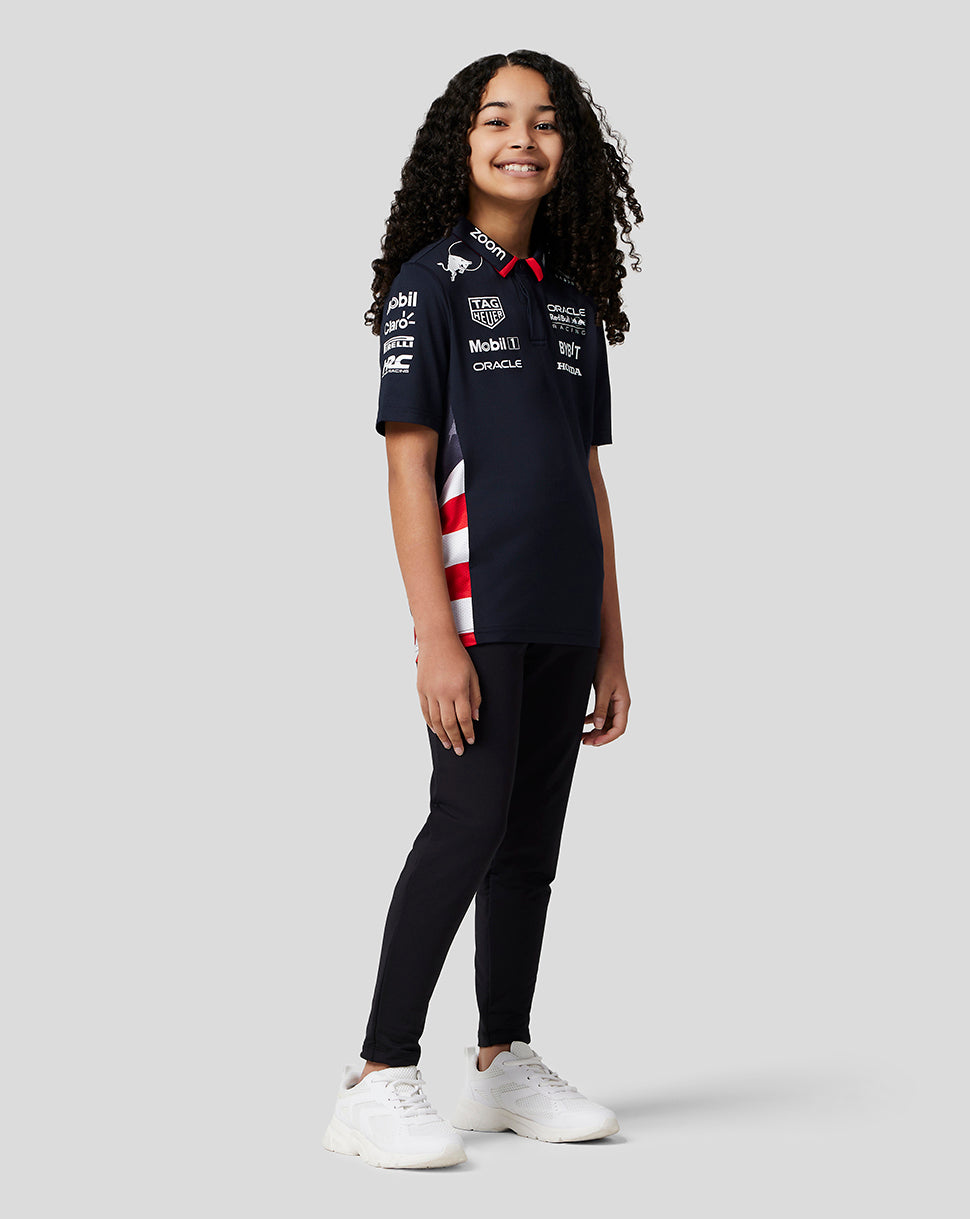 Young model wearing a navy Oracle Red Bull Racing Junior Teamline polo with sponsor logos on the chest and sleeves