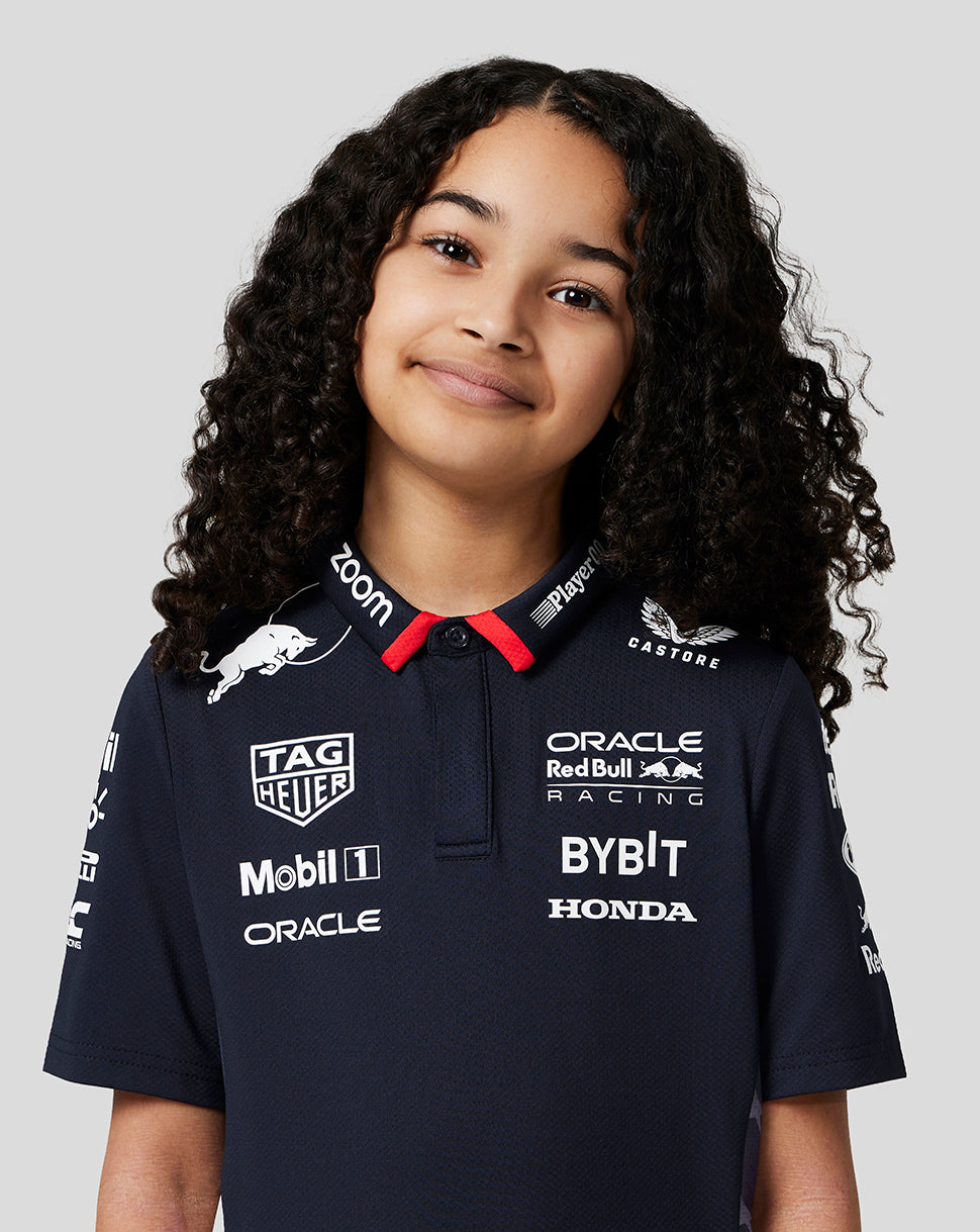 Front view of a smiling girl in a navy Red Bull Racing polo covered in sponsor logos.
