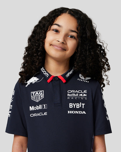 Front view of a smiling girl in a navy Red Bull Racing polo covered in sponsor logos.