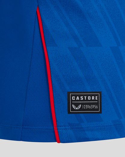 Close-up of blue Rangers Junior home long sleeve shirt showing red piping along the side seam and Castore label patch.