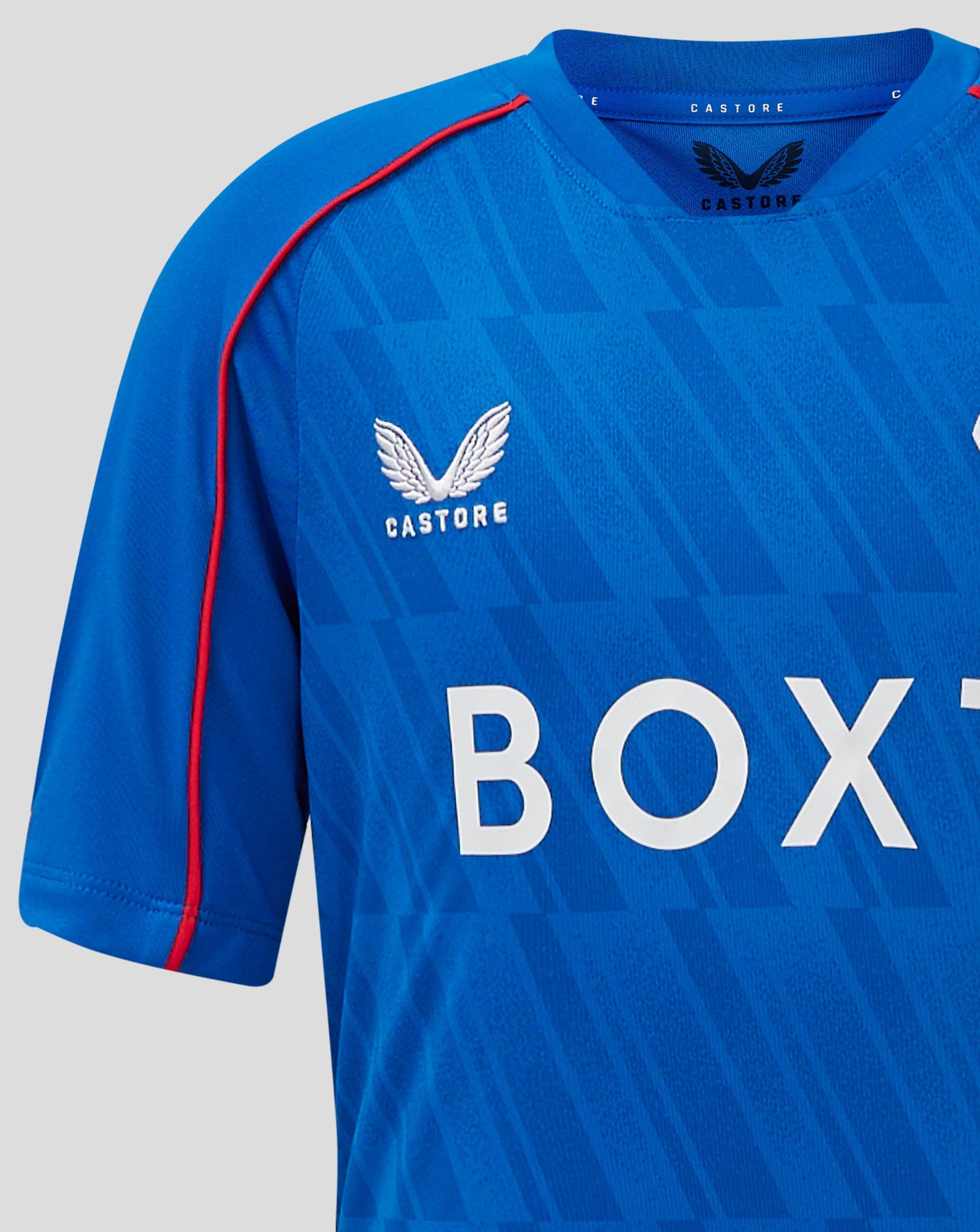 Blue Rangers Junior Home Shirt close up showing Castore branding at the neck, piping along the shoulder, and the Rangers crest on the left chest.