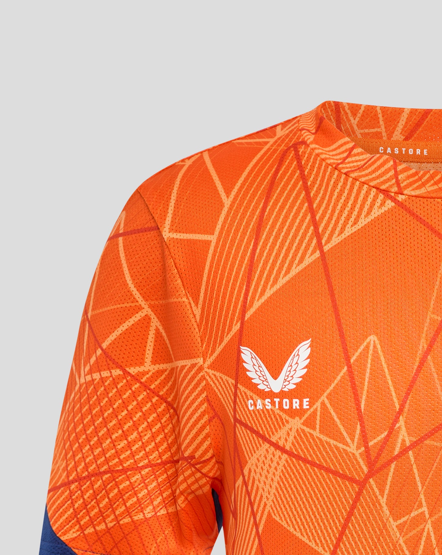 Close up of orange Rangers 24/25 Junior League Matchday T Shirt fabric with white geometric lines and Castore label at the collar.