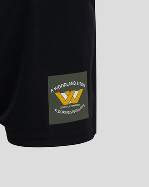 Close-up of the lower left leg of the shorts showing a Woodland & Son logo patch